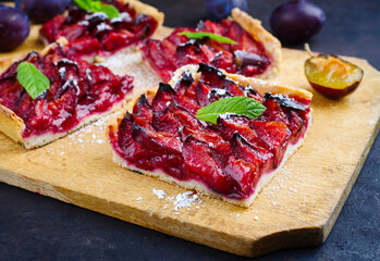 Traditioneller deutscher Zwetschgenkuchen mit aufgeschnittenen Pflaumen serviert als close-up auf einem rustikalen Holzbrett