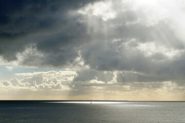Morning over the ocean. The clouds and the sun breaks through the thick veil. A distant yacht in the rays of sunlight. Glare on the water