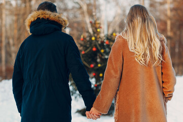 Fototapeta premium Young adult couple walking near christmas tree in winter forest. New year pine holiday party celebration concept