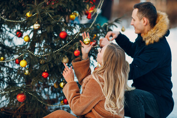 Young adult couple decorates christmas tree in winter forest. New year pine holiday party celebration concept
