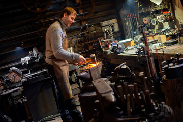 Fototapeta na wymiar The blacksmith manually forging the red-hot metal on the anvil in smithy with spark fireworks