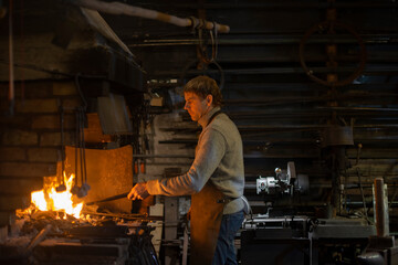 Latvian  blacksmith working with open fire in furnace. The blacksmith forging hot iron in workshop