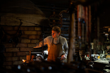 Obraz premium Latvian blacksmith working with open fire in furnace. The blacksmith forging hot iron in workshop