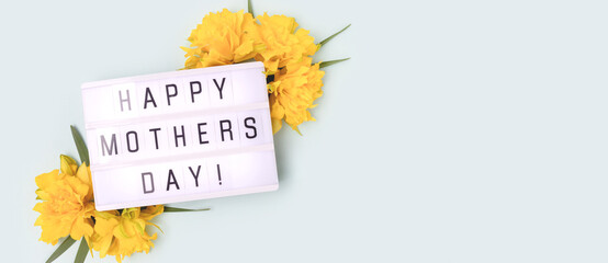 Naklejka premium Happy Mothers Day. Banner with lightbox with quote and frame made of yellow narcissus on a blue pastel background.