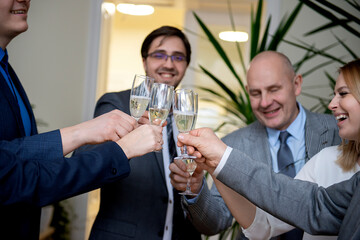 Successful business people are clinking glasses of champagne and smiling while celebrating in office