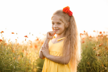 Cheerful girl with a smile on her face in blooming field poppies. Red flowers. A blonde in a yellow short dress and a hat.