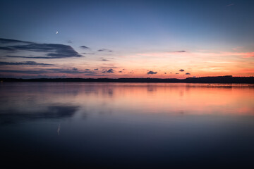Beautiful sunset on the lake, reflection of clouds and moon, background