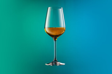 Image of white wine glass isolated over gradient blue and green color background in neon. Concept of alcohol, holidays, New Year