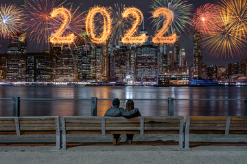2022 written with Sparkle firework with multicolor of fireworks on back side couple sitting and looking New york Cityscape background, USA downtown skyline,Happy new year and merry Christmas concept - obrazy, fototapety, plakaty