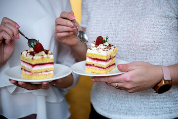 close-up of two women's hands eating  cream cake decorated with berries