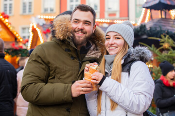 Beautiful couple eating czech Trdelnik on Christmas fair in Wroclaw, Poland