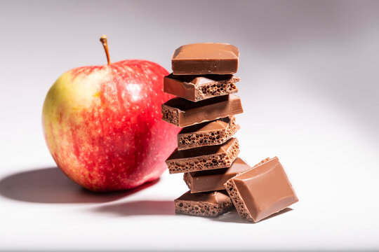 Brown Porous Chocolate In The Foreground On The Background Of An Apple On A White Table.