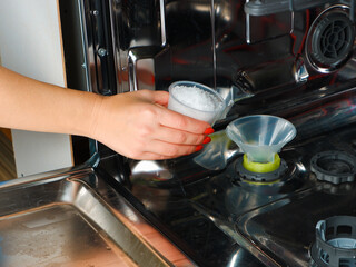 Adding salt to the dishwasher. A woman's hand pours salt to soften the water into the dishwasher. Dishwasher salt for regenerating the water softener