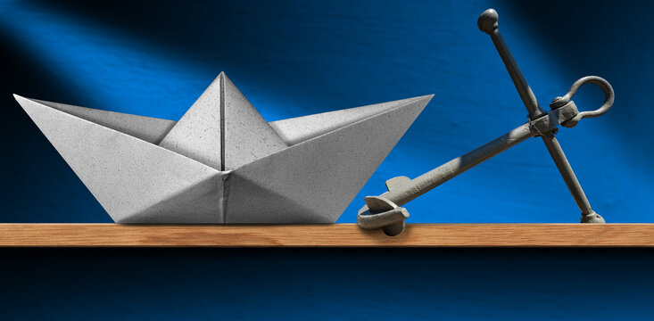 Close-up of a white paper boat and a gray metal anchor on a wooden shelf at home, with a blue wall on background.