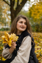 girl model holding yellow leaves in her hand. photo session of the girl in the autumn park. model appearance, beautiful smile, side glance.