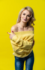 Studio portrait of beautiful blonde woman. model in a yellow sweater and blue jeans poses for the camera. yellow, colored background