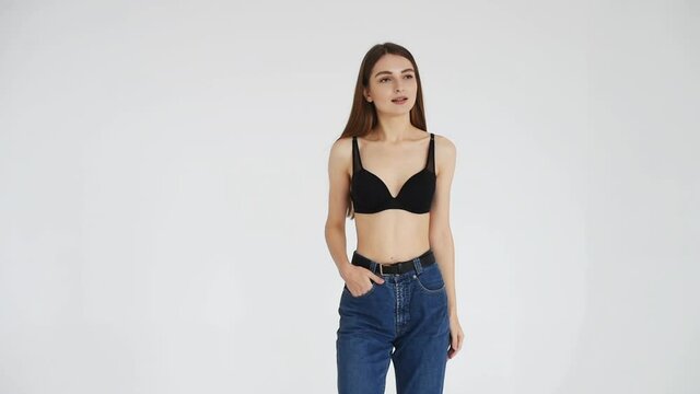 Young woman in jeans and white bra against white background