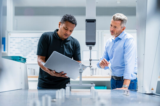 Engineer discussing over laptop with businessman in factory