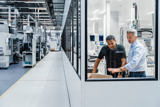 Businessman explaining strategy on laptop to engineer in factory