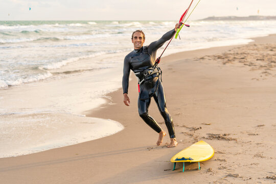 Smiling man holding rope of parachute by kiteboard at beach