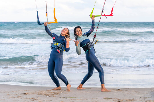 Cheerful friends gesturing and kitesurfing at beach