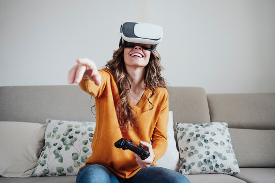 Woman with joystick gesturing wearing virtual reality headset at home