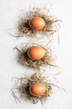 Studio shot of three chicken eggs lying on hay against white background