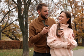 Happy couple wearing stylish clothes with cups of coffee in autumn park