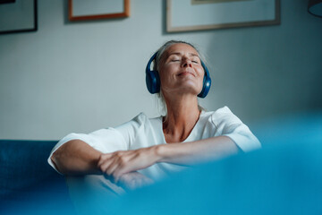 Smiling woman listening music through headphones at home