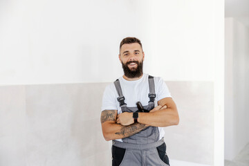 A hardworking, successful bearded painter is standing proudly with arms crossed in the freshly...