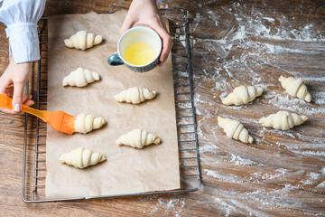 The cook greases egg croissants on the table with ingredients.