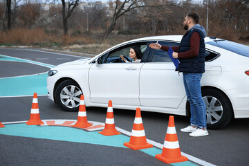 Instructor near car with his student during exam at driving school test track
