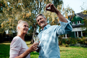 Smiling man holding champagne flute and house key by woman at backyard