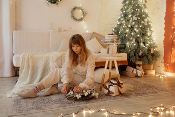 Young stylish girl in warm clothes decorates the christmas tree and decorates the room. New year...