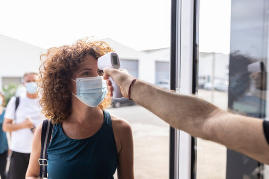 Man taking temperature of woman wearing protective face mask at doorway