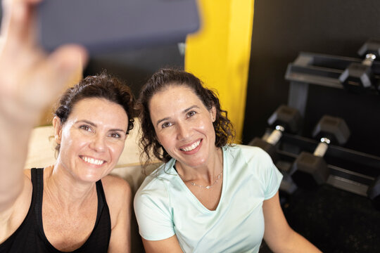 Smiling woman taking selfie with friend through mobile phone in gym