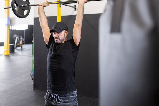 Sportsman with arms raised deadlifting in gym