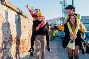 Cheerful man and woman piggybacking friends on footpath