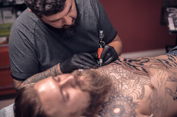 Professional tattoo artist does tattoo on the skin of his client in a workshop studio