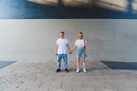 Lesbian couple with multi colored face mask holding hands on footpath