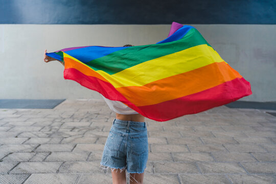 Woman with denim shorts holding rainbow flag on footpath