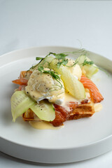 Salmon and poached egg waffle with hollandaise sauce, top view on white dish, menu design