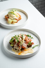 Two portions of waffle breakfast with smoked salmon and poached eggs, top view on white table, copy space menu photo