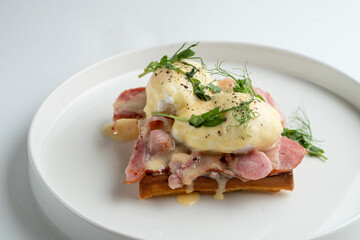 Prosciutto and poached egg waffle, appetizing photo, top view on white restaurant table