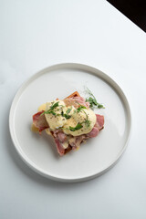 Prosciutto and poached egg waffle, appetizing photo, top view on white restaurant table