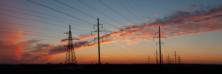 Electric Energy. Industrial landscape. Several high voltage power lines on high poles. Evening sky with unusual clouds