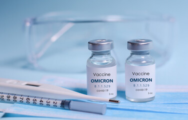 Two Bottle of Covid-19 vaccine to immunize from the Omicron Variant Coronavirus, syringe , face mask,body thermometer and protective glasses on blue background.The concept of medicine, healthcare
