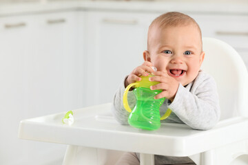 Cute little baby with sippy cup at home. Space for text