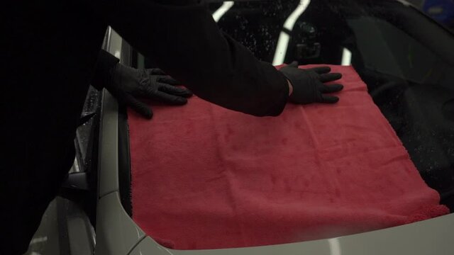 Man after washing wipes white car with a rag at car wash. Male hand and car body close up.