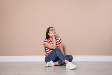 Young woman sitting on floor near beige wall indoors - Powered by Adobe